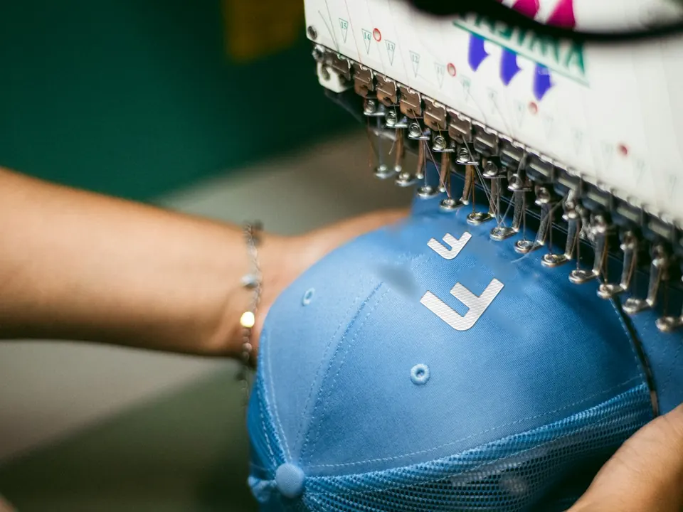 Máquina de bordar de varias agujas bordando las dos F del logo de Fun Fashion en una gorra azul